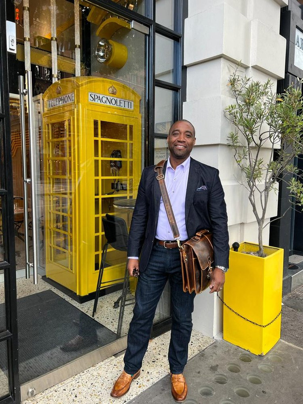 A man in a suit and tie for alterations standing in front of a yellow phone booth